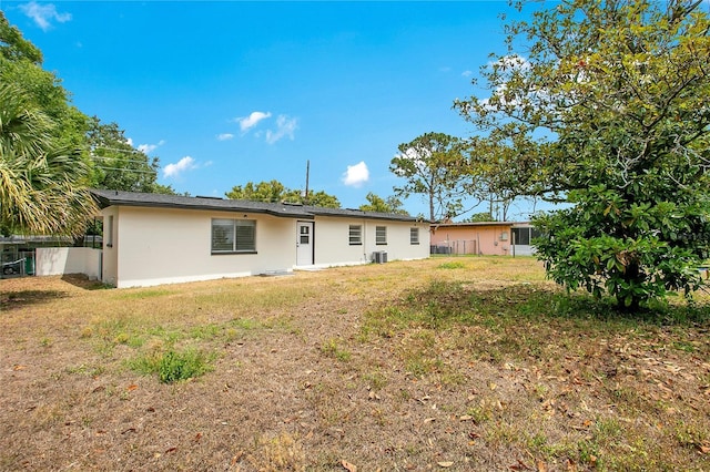 rear view of property featuring stucco siding, fence, a lawn, and central AC unit