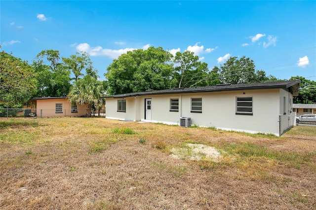 rear view of house with a lawn, central air condition unit, and fence