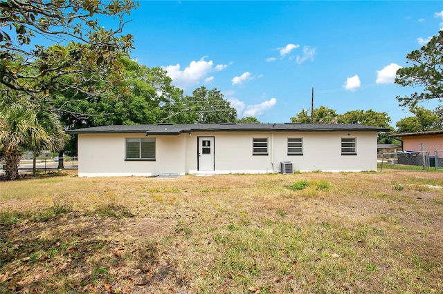 back of house featuring central AC, fence, stucco siding, and a lawn