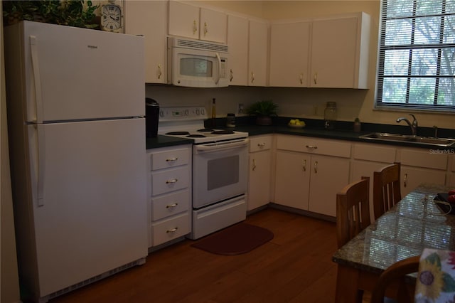 kitchen featuring dark countertops, a sink, dark wood-style floors, white appliances, and white cabinetry