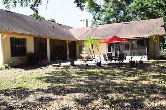 back of property with roof with shingles, a chimney, a patio area, and stucco siding