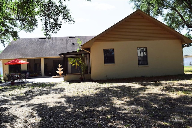 rear view of property featuring a shingled roof, a patio area, and stucco siding