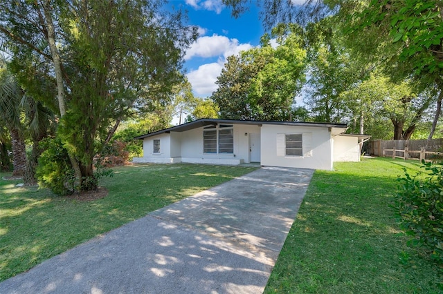 view of front of house with driveway, fence, a front yard, and stucco siding