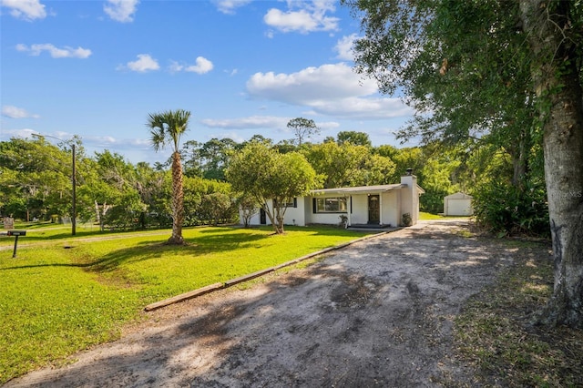 view of front of house featuring a front lawn, an outdoor structure, driveway, a chimney, and stucco siding