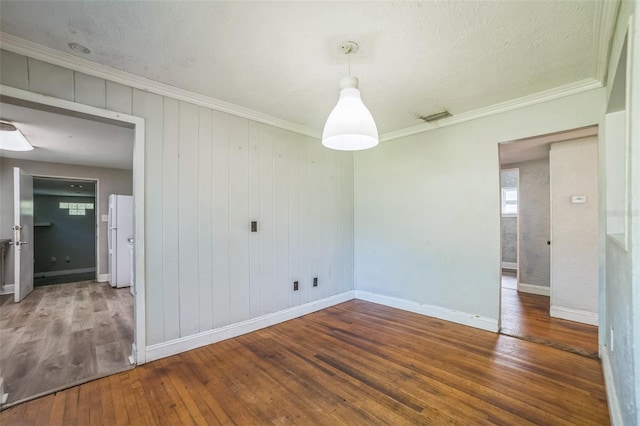 empty room featuring baseboards, visible vents, hardwood / wood-style floors, and crown molding