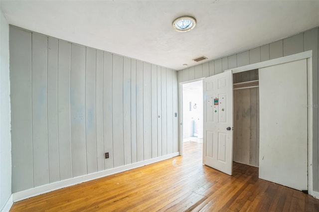 unfurnished bedroom with wooden walls, a closet, hardwood / wood-style floors, and visible vents