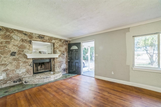 unfurnished living room with a textured ceiling, hardwood / wood-style flooring, baseboards, ornamental molding, and a stone fireplace