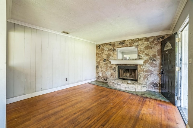 unfurnished living room with hardwood / wood-style floors, a stone fireplace, visible vents, a textured ceiling, and crown molding
