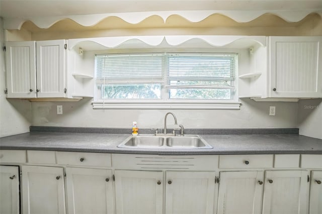 kitchen featuring dark countertops, open shelves, white cabinets, and a sink