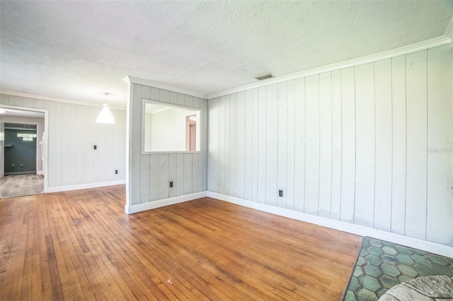unfurnished room with visible vents, hardwood / wood-style flooring, ornamental molding, and baseboards