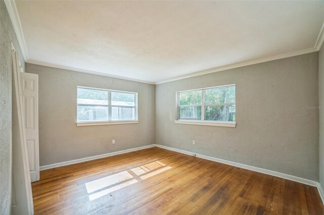 empty room featuring crown molding, hardwood / wood-style floors, and baseboards