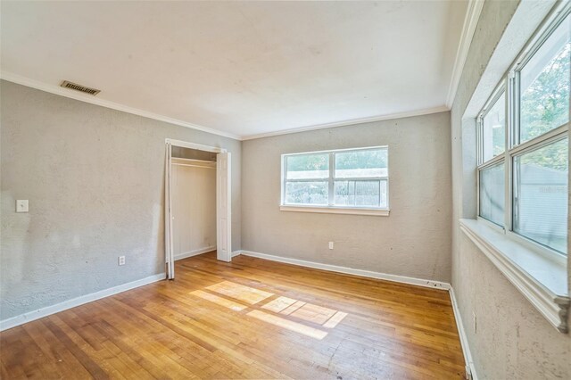 unfurnished bedroom with hardwood / wood-style flooring, a closet, baseboards, visible vents, and crown molding