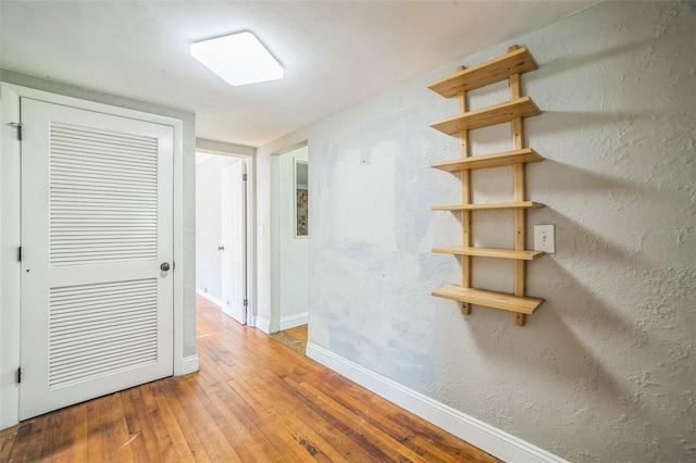 corridor featuring a textured wall, hardwood / wood-style flooring, and baseboards