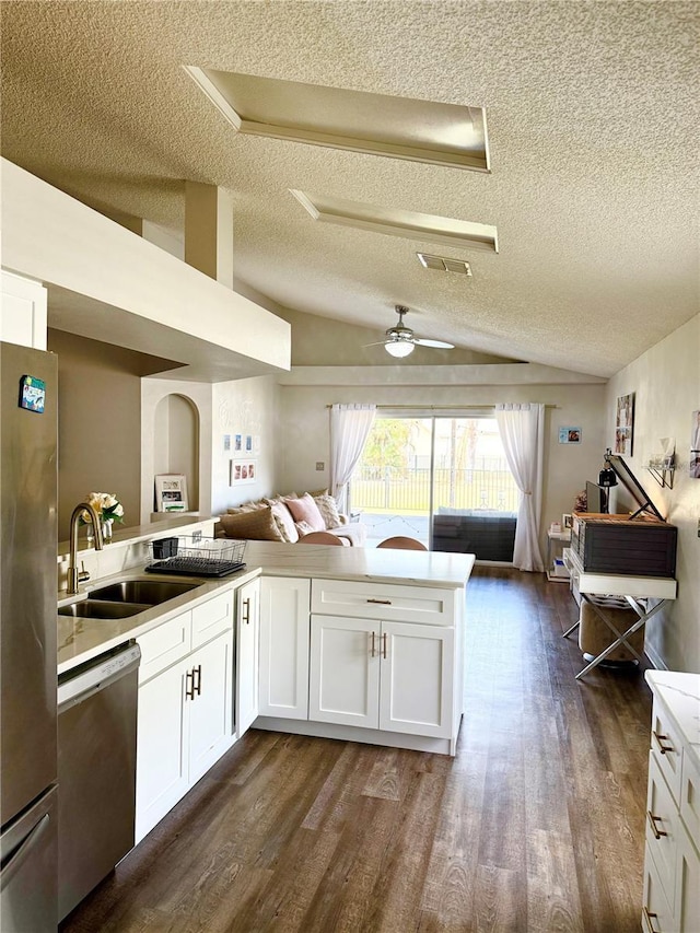kitchen with a textured ceiling, appliances with stainless steel finishes, vaulted ceiling, a sink, and open floor plan