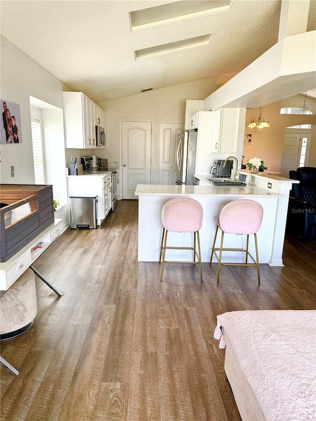 kitchen with a breakfast bar area, stainless steel appliances, dark wood finished floors, and lofted ceiling