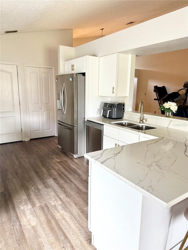 kitchen featuring light stone countertops, white cabinets, a sink, light wood finished floors, and stainless steel appliances