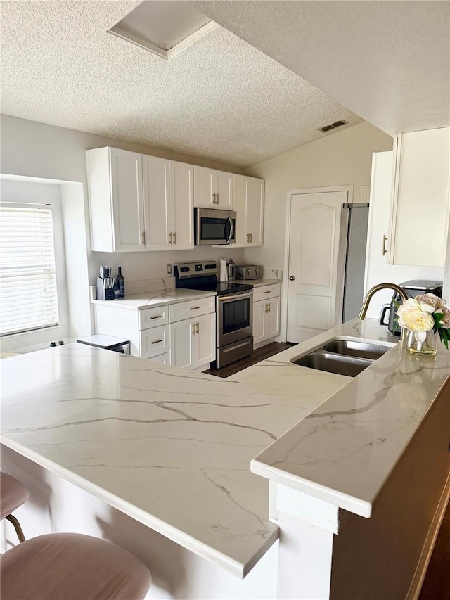 kitchen featuring white cabinets, appliances with stainless steel finishes, a sink, a breakfast bar area, and a textured ceiling