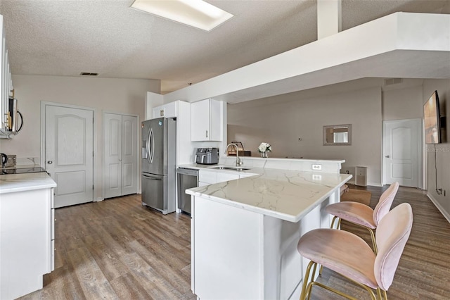 2407 Oakington St, Winter Garden, FL 34787 - kitchen with appliances with stainless steel finishes, a peninsula, a sink, light wood-style floors, and white cabinets