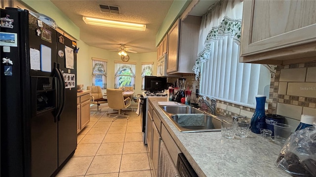 kitchen featuring a sink, light tile patterned flooring, black fridge, tasteful backsplash, and range with gas cooktop