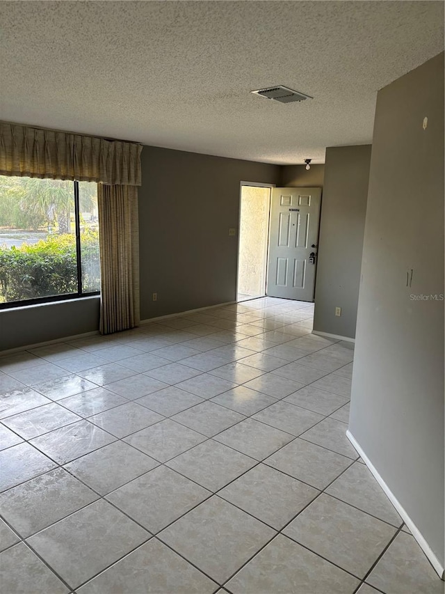 spare room featuring light tile patterned floors, a textured ceiling, and baseboards
