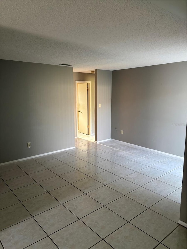 spare room with light tile patterned floors, a textured ceiling, and baseboards