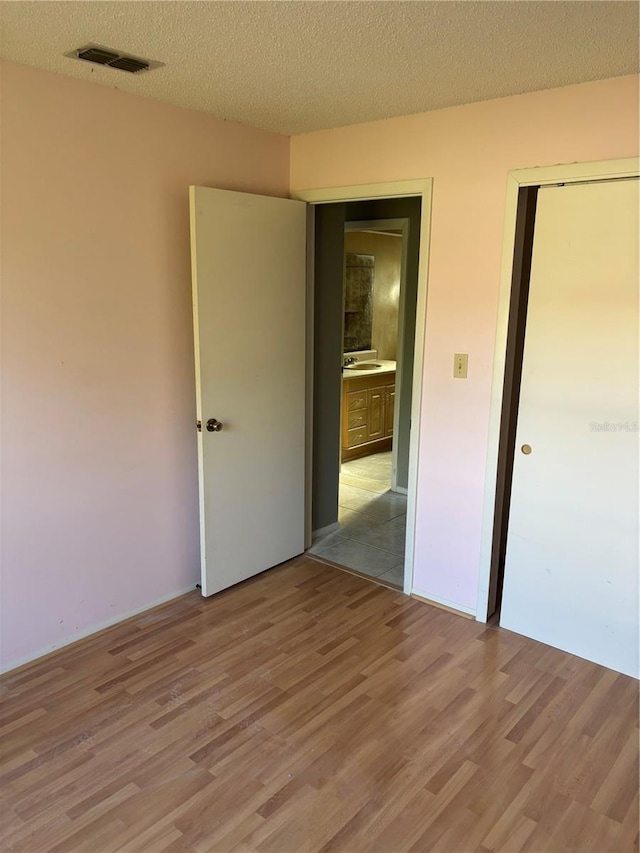 unfurnished bedroom with a sink, a textured ceiling, visible vents, and light wood-style floors