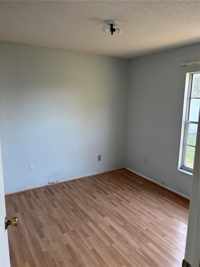 unfurnished room featuring a textured ceiling, baseboards, and light wood-type flooring