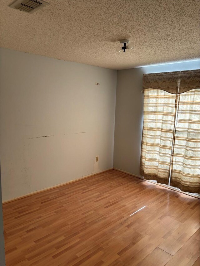 unfurnished room with wood finished floors, visible vents, and a textured ceiling