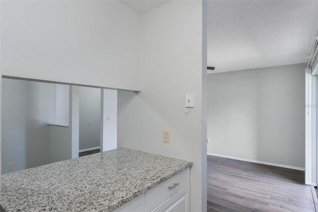 kitchen featuring light stone countertops, a textured ceiling, white cabinetry, baseboards, and wood finished floors