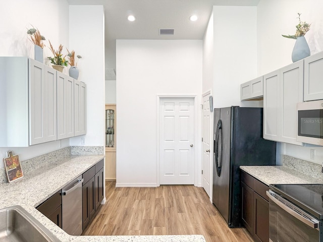 kitchen featuring light wood-type flooring, a towering ceiling, appliances with stainless steel finishes, and visible vents