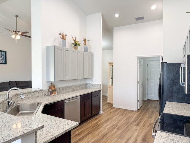 kitchen featuring a ceiling fan, light stone countertops, light wood-type flooring, a sink, and stainless steel appliances