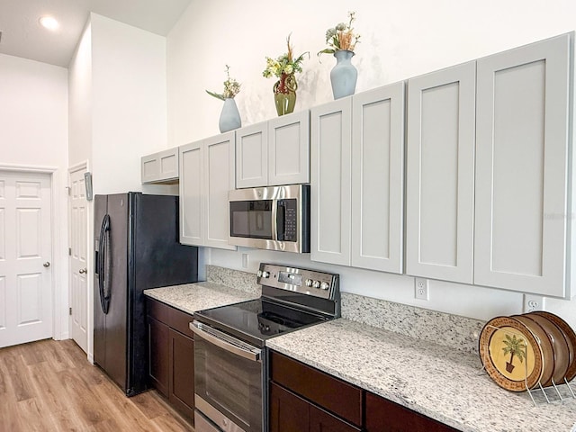 kitchen with dark brown cabinetry, appliances with stainless steel finishes, light wood-type flooring, light stone counters, and recessed lighting
