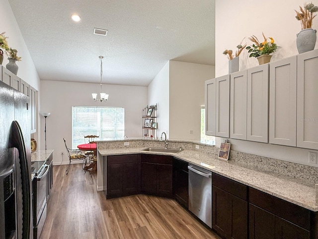 kitchen with a sink, light wood-style floors, a chandelier, stainless steel appliances, and a peninsula