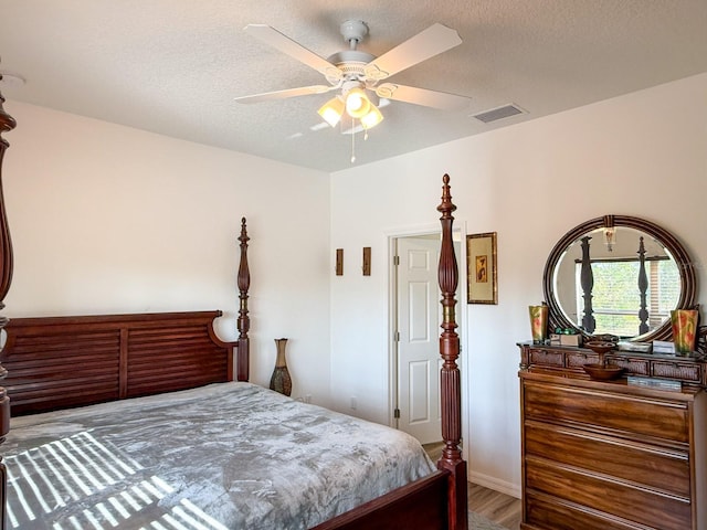 bedroom with ceiling fan, a textured ceiling, baseboards, wood finished floors, and visible vents