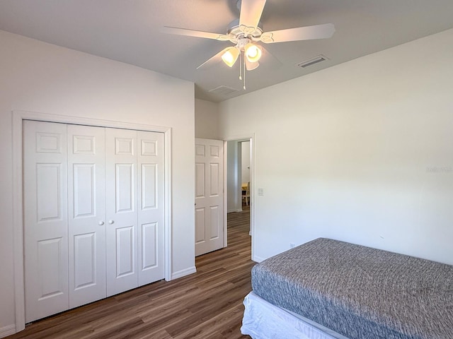 bedroom with ceiling fan, visible vents, wood finished floors, baseboards, and a closet