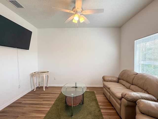 living room featuring ceiling fan, a textured ceiling, visible vents, and wood finished floors