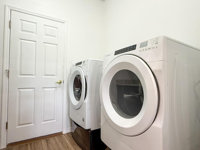 clothes washing area featuring laundry area, washer and clothes dryer, and wood finished floors