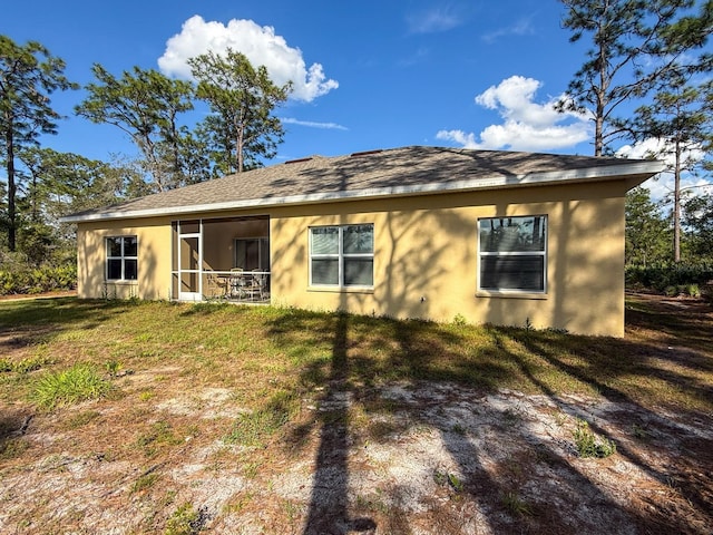 rear view of property featuring a yard, stucco siding, and a sunroom
