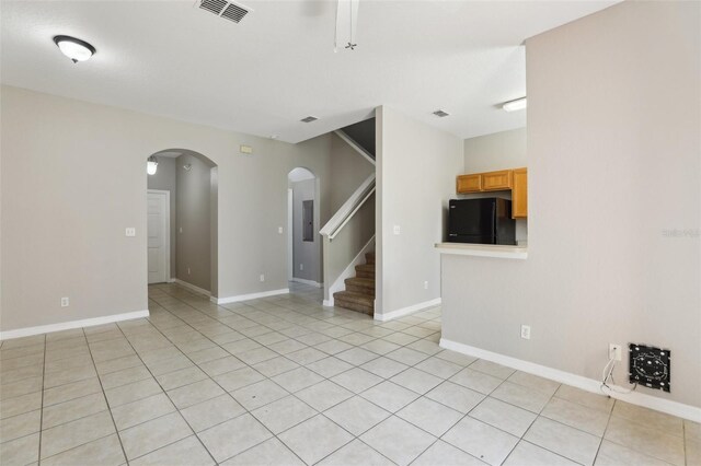 unfurnished living room featuring arched walkways, visible vents, light tile patterned floors, and stairway