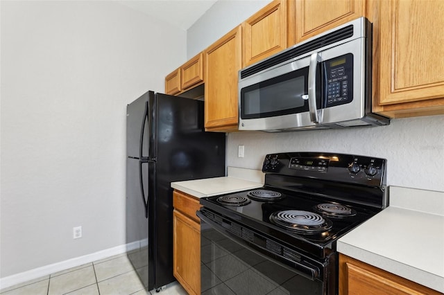 kitchen with baseboards, light countertops, light tile patterned floors, and black appliances