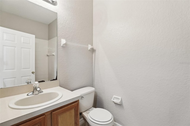 bathroom featuring toilet, a textured wall, and vanity