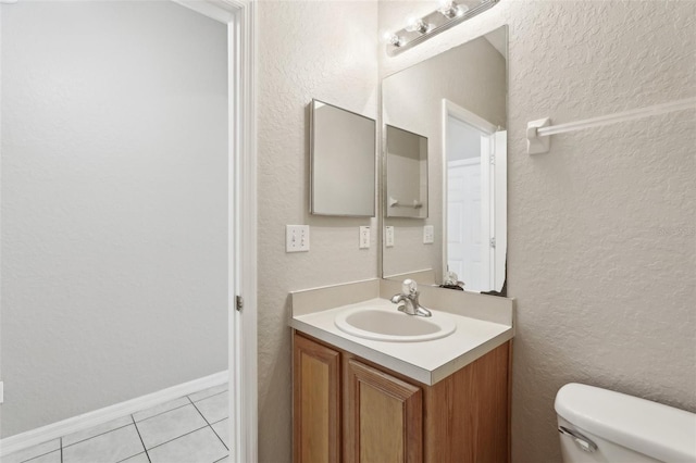 bathroom featuring vanity, tile patterned flooring, a textured wall, and toilet