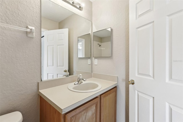 bathroom featuring vanity, a textured wall, and toilet