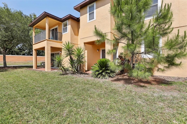 view of property exterior with a yard, a balcony, and stucco siding