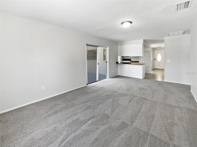 unfurnished living room with baseboards, light colored carpet, a textured ceiling, and visible vents