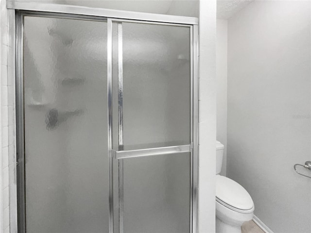 bathroom featuring baseboards, a stall shower, and toilet