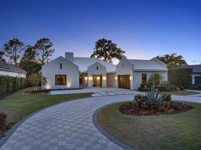 view of front of house with a chimney, curved driveway, a front lawn, an attached garage, and stucco siding