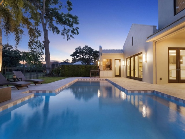 pool at dusk with fence, french doors, and a patio area