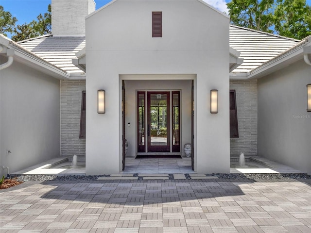 property entrance featuring brick siding, a chimney, a tile roof, and stucco siding