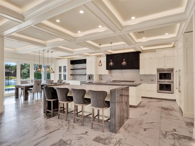 kitchen featuring visible vents, open shelves, a large island with sink, double oven, and coffered ceiling